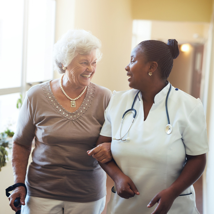 Nurse Walking with Elderly Woman caretaker walks down hall with elderly woman